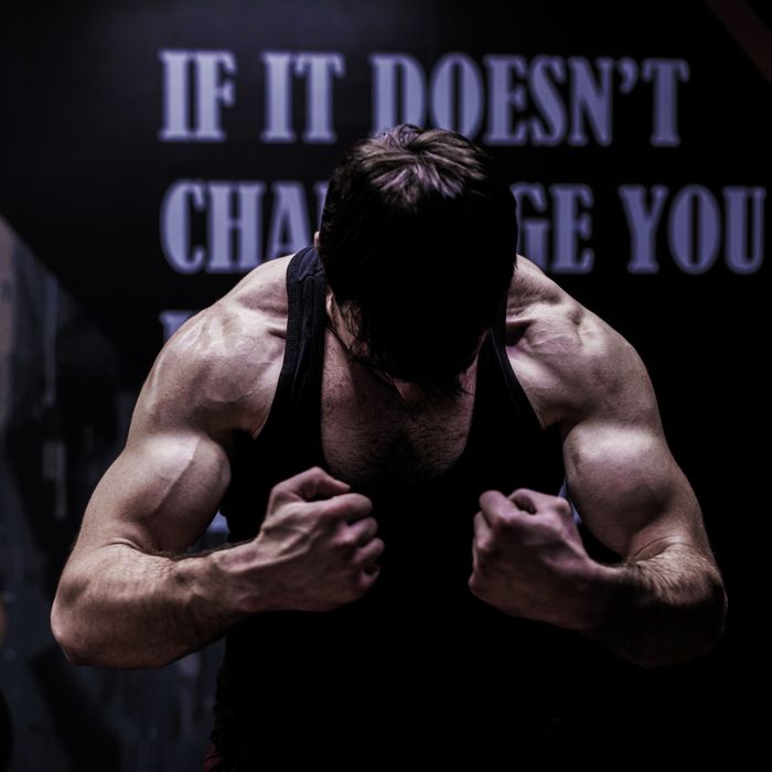 hero-about Muscular male bodybuilder posing in a dimly lit gym, showcasing strength and dedication.