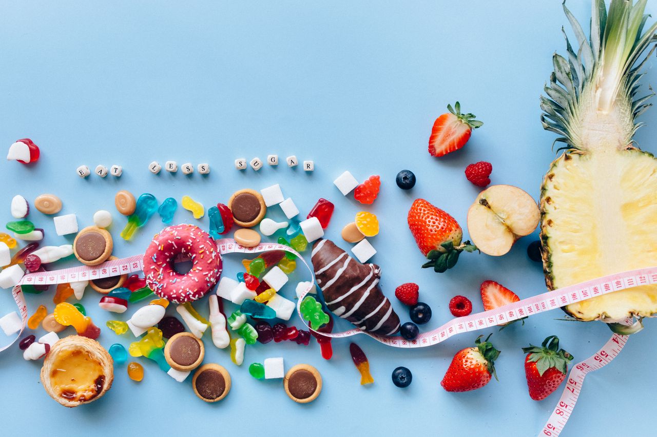 services-02 Flat lay of sweets and fruits on blue background with health message 'Eat Less Sugar'.