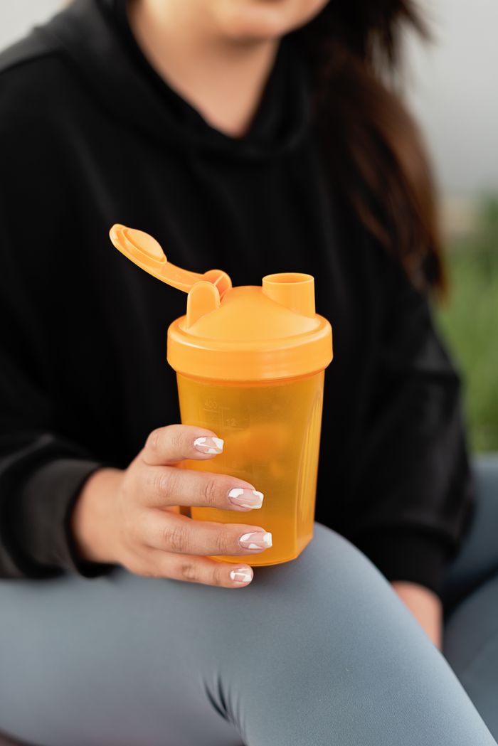 services-03 Close-up of a woman holding an orange shaker bottle. Ideal for fitness and hydration themes.